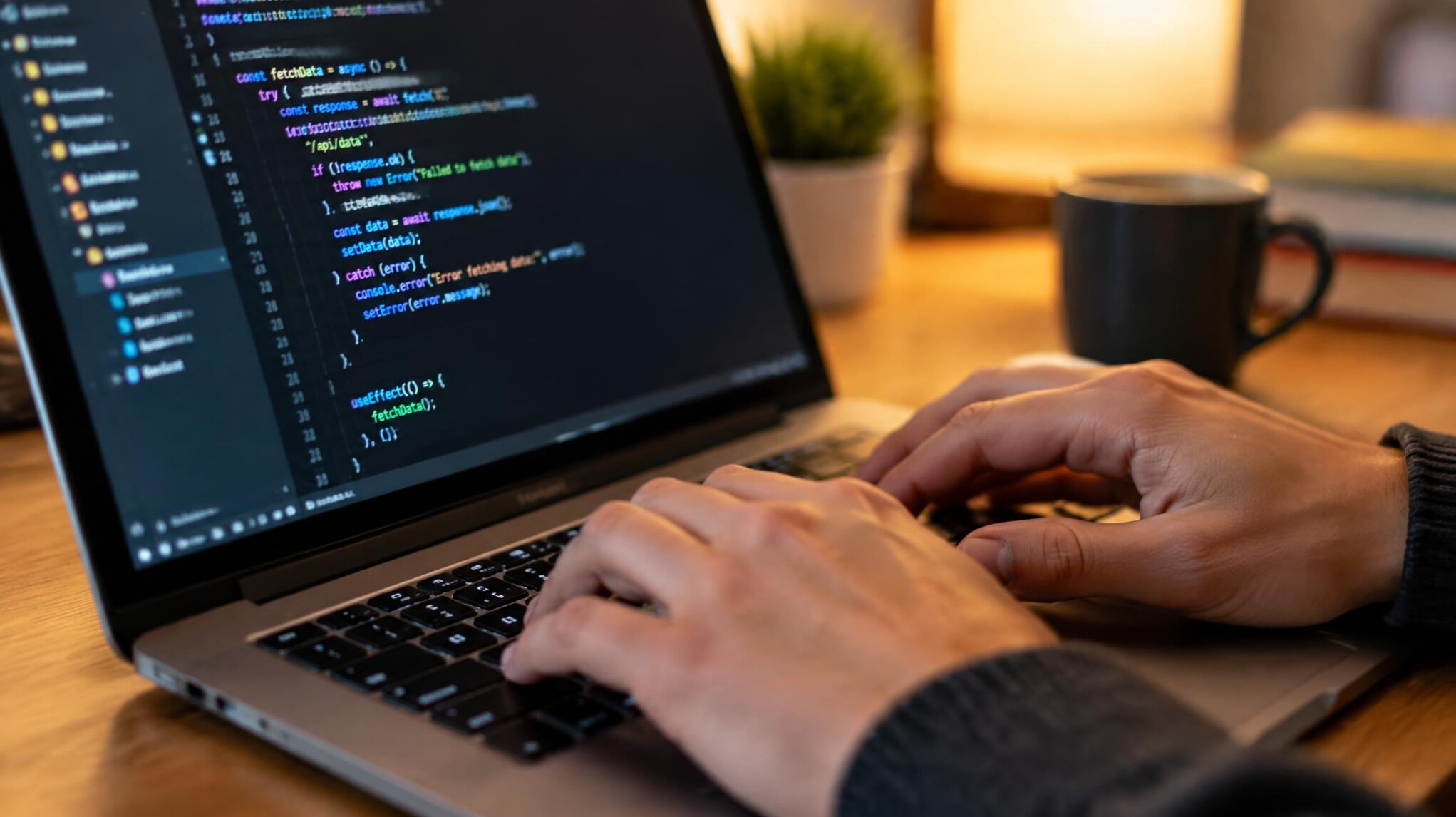 Close up of hands typing on a laptop keyboard with code on screen